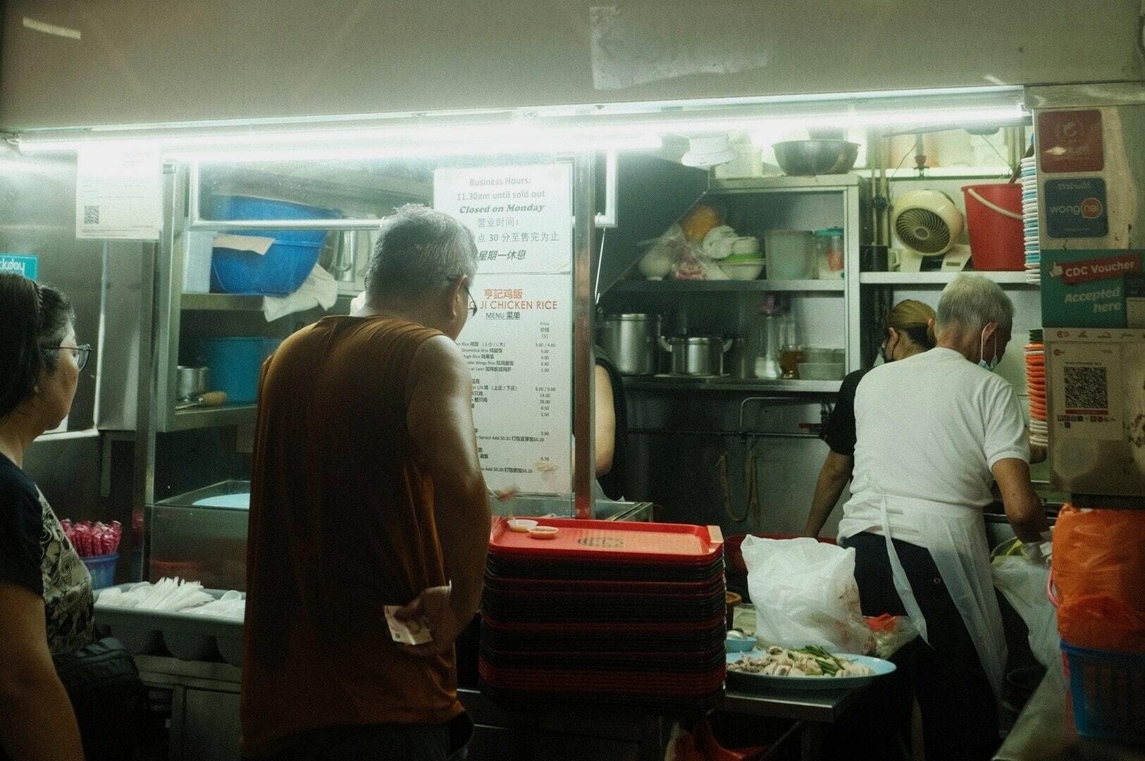 People gathered in front of a vibrant Singapore Hawkers food stand, enjoying local cuisine.