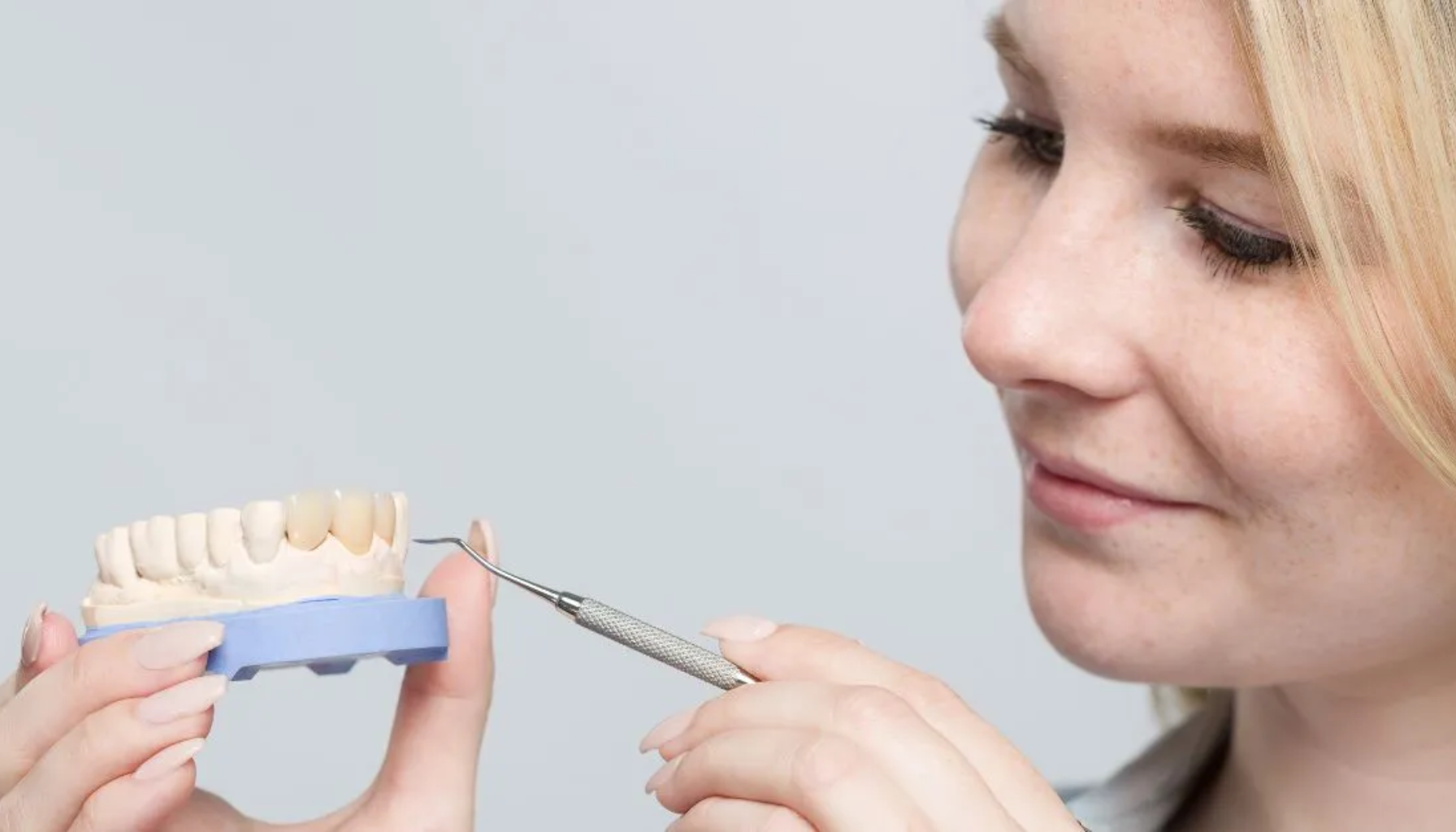 All-on-4: Tannløsningen Som Forandrer Livet Ditt På Én Dag 15 Kvinne som arbeider med en tannmodell og bruker et tannlegeverktøy for å forme eller kontrollere tennene, med fokusert uttrykk og nøyaktighet.