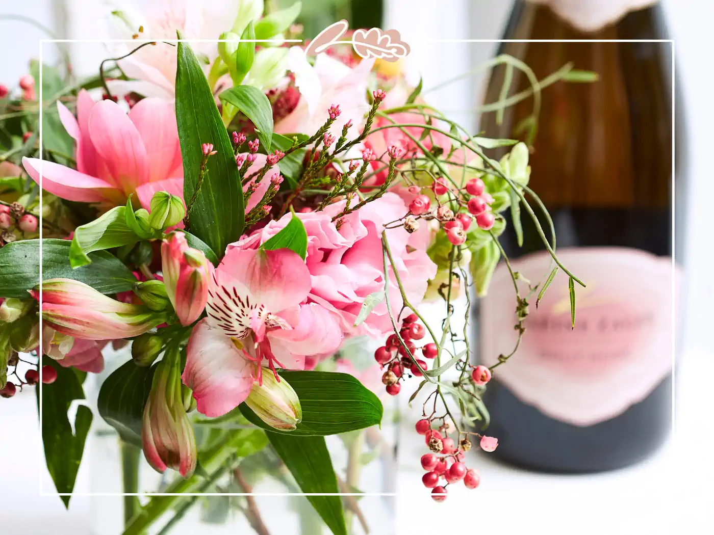 A charming bouquet of pink flowers in a glass vase, paired with a bottle of sparkling wine. Fabulous Flowers and Gifts.