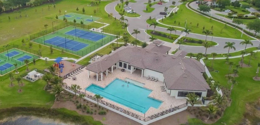 An aerial view of the Portico gated community in Fort Myers, FL, showcases stunning lakefront residences surrounded by mature trees and natural preserves, highlighting the beautiful amenities such as the fitness center, basketball court, and pool. The image captures the essence of this highly desired community, ideal for families seeking exquisite modern luxury and a serene living environment.