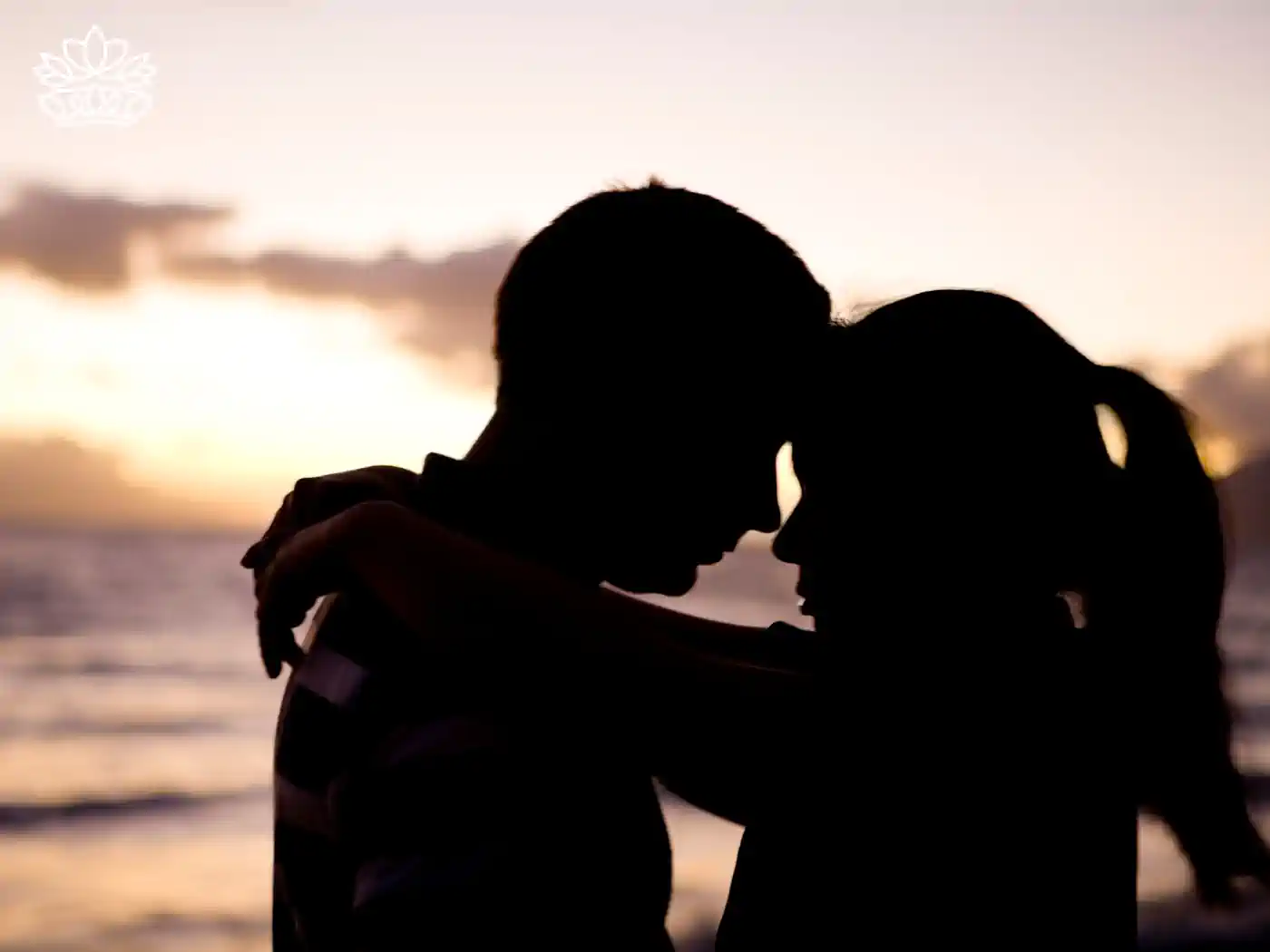 Silhouette of a couple embracing at sunset by the sea, representing the Romance Collection. Fabulous Flowers and Gifts.