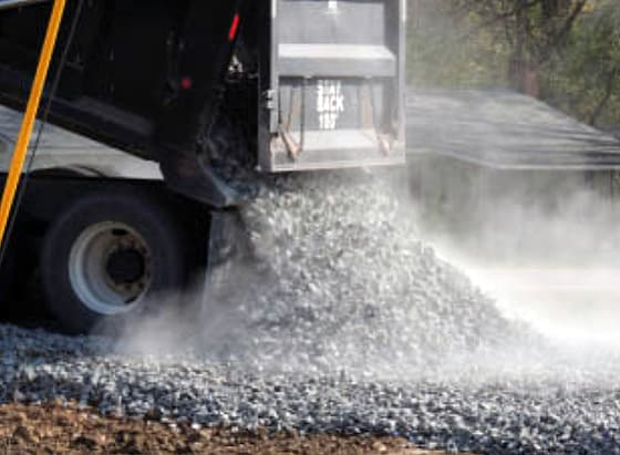 A photo of a dump truck unloading small rocks and asphalt for a parking lot paving job