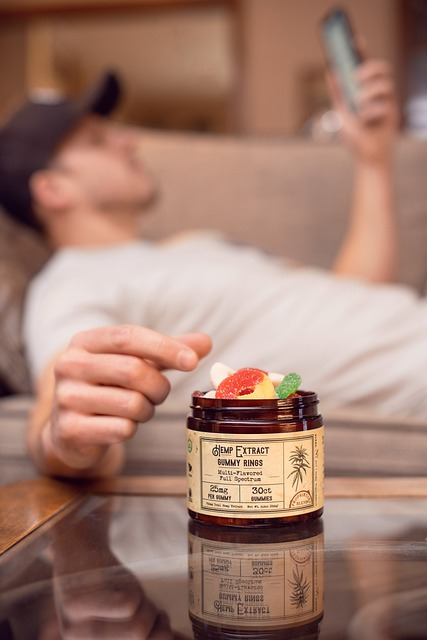 man lying on the sofa on his phone reaching out to take microdose gummies, candy, edibles