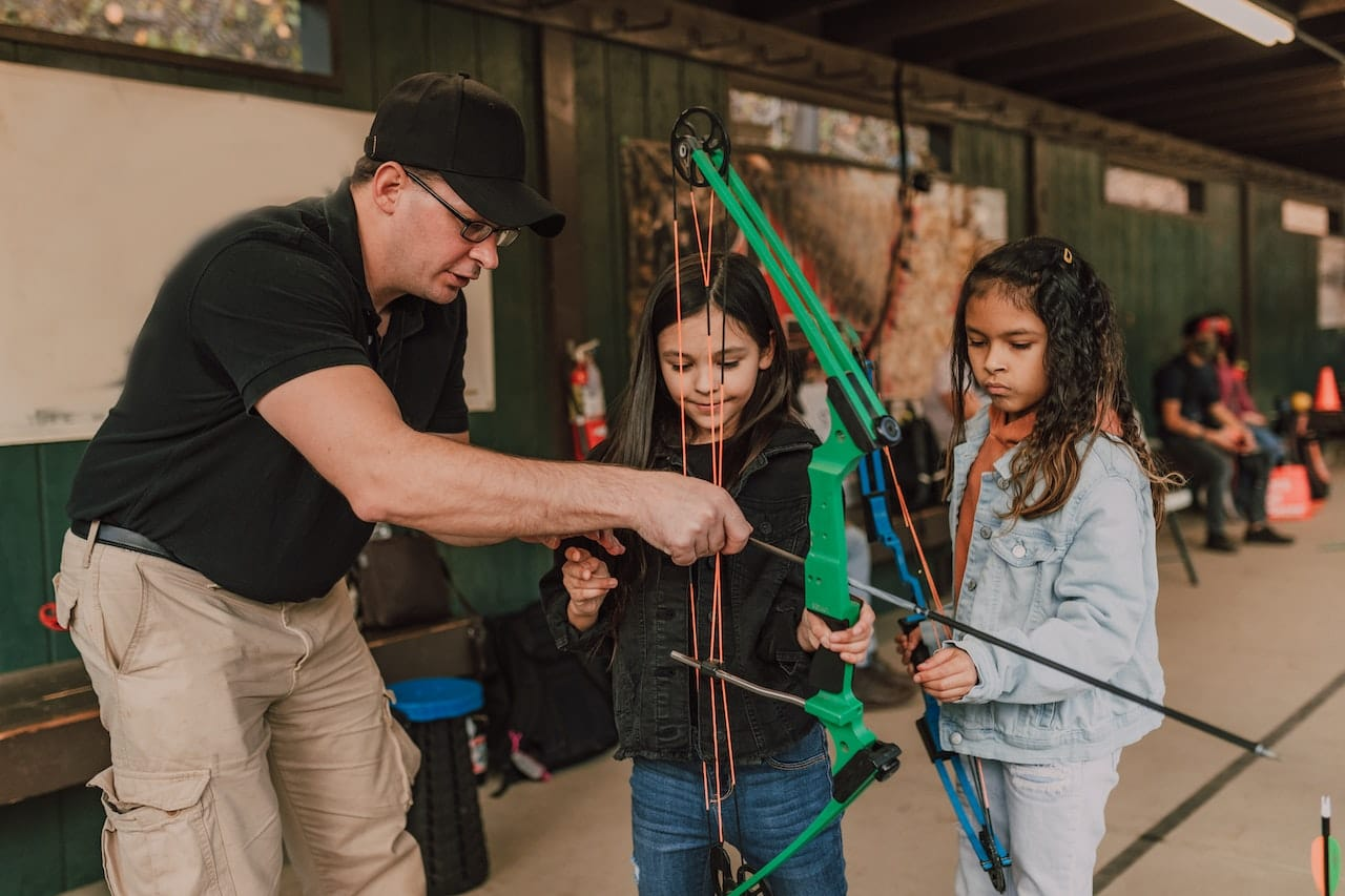Children learning to handle a youth compound bow.