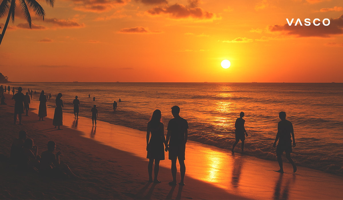 A couple watching a beautiful orange sunset on a beach in Bali, with silhouettes of other people around.