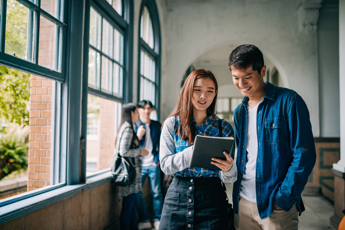 Filipino university students reviewing a tablet in a campus hallway, representing direct outreach and early recruitment.
