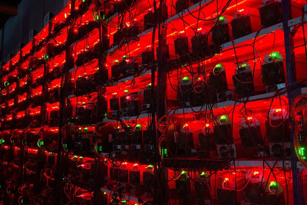 An image of multiple Bitcoin mining rigs with bright lights.