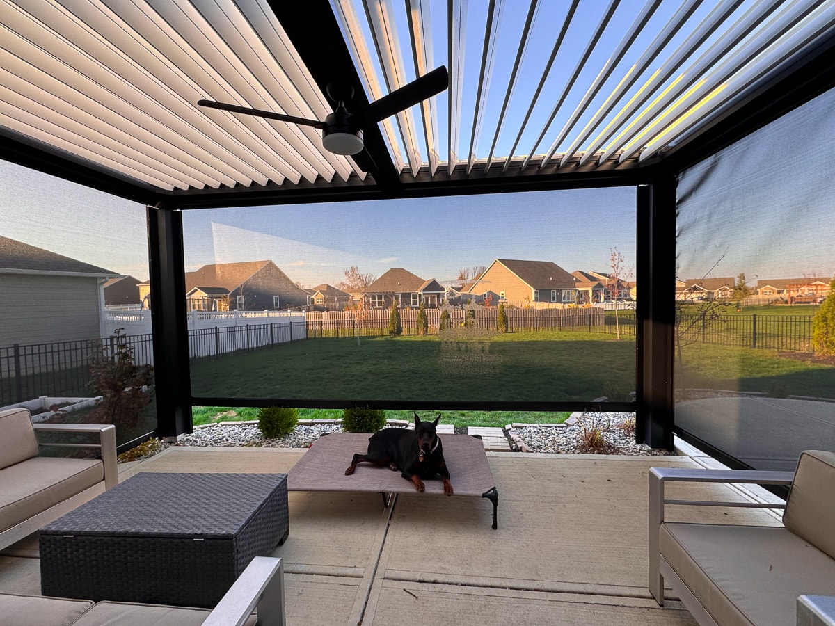 A pergola with three screens, installed over a patio, with outdoor furniture.
