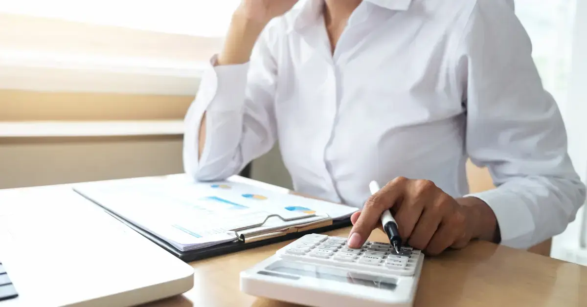 Woman in her home office, calculating how to pay less in taxes with tax forms and a calculator.