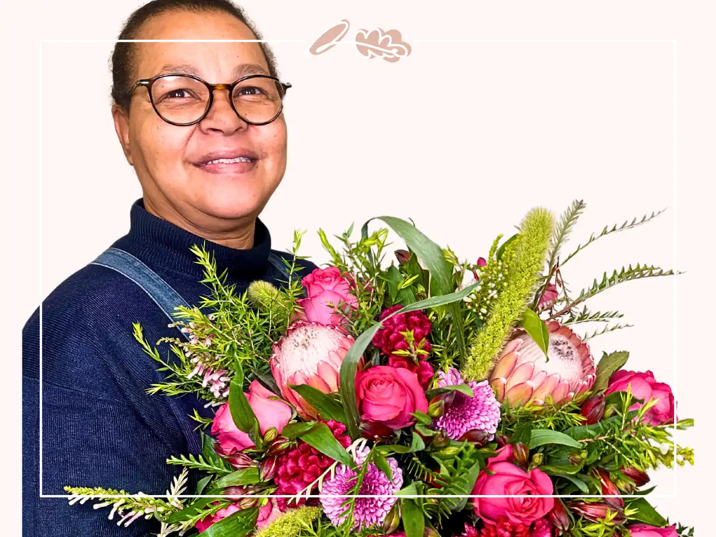 Florist with glasses and a dark blue sweater, holding a large bouquet of pink and green flowers, smiling warmly at the camera - Fabulous Flowers and Gifts