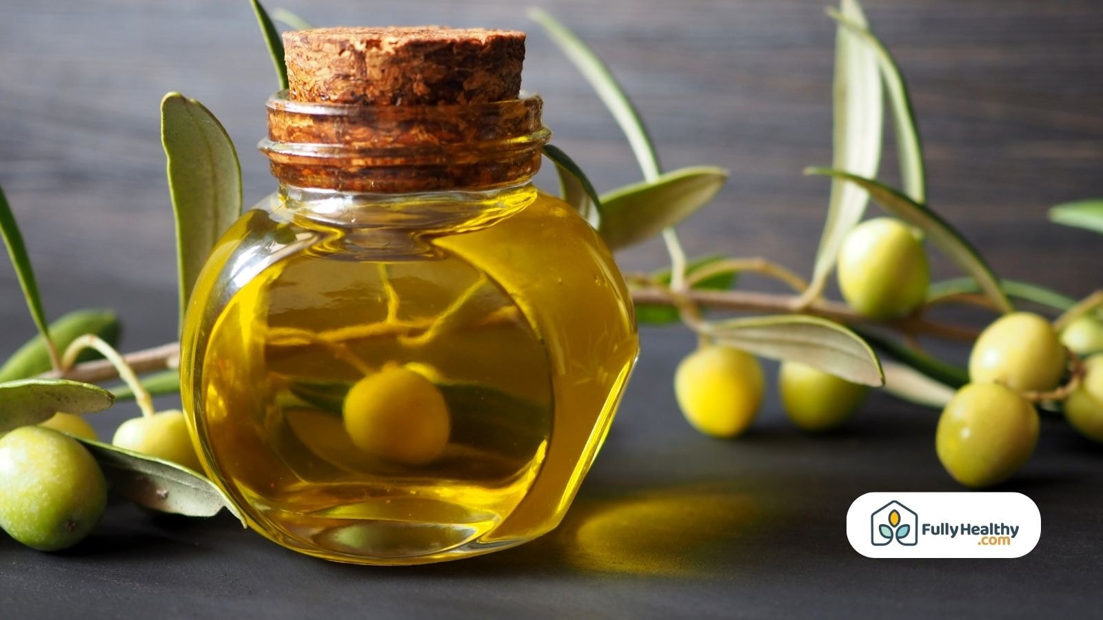 Small glass jar of olive oil with olive branch and green olives