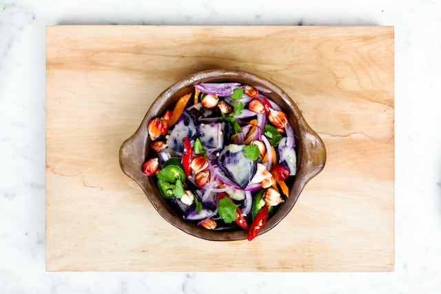 A vegetable salad bowl on a light brown chopping board