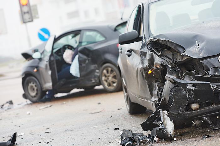 Two severely damaged cars at a collision scene, with one vehicle's front end completely crumpled and the other showing an open door with a deployed airbag, illustrating the serious injuries that can result from Texas car accidents.