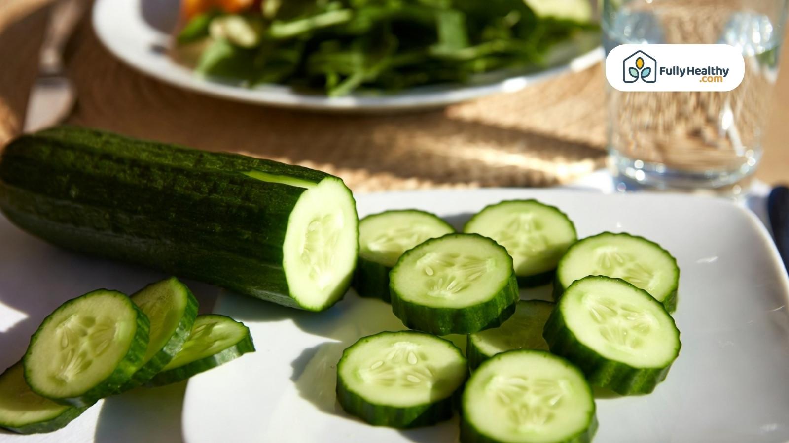 Sliced cucumber rounds on plate in sunlight, with glass and greens behind