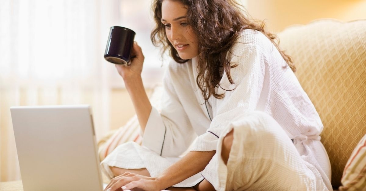 A woman working from home on a laptop, searching for IRS tax solutions while holding a coffee cup.