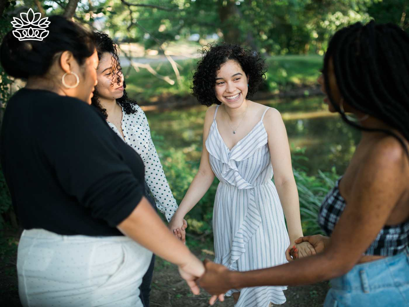 Four friends joyfully holding hands in a circle in a lush park setting, sharing a moment of happiness and connection. Perfect for celebrating their bond with gift sets that include makeup from the Gifts Boxes for Women Collection. Fabulous Flowers and Gifts.