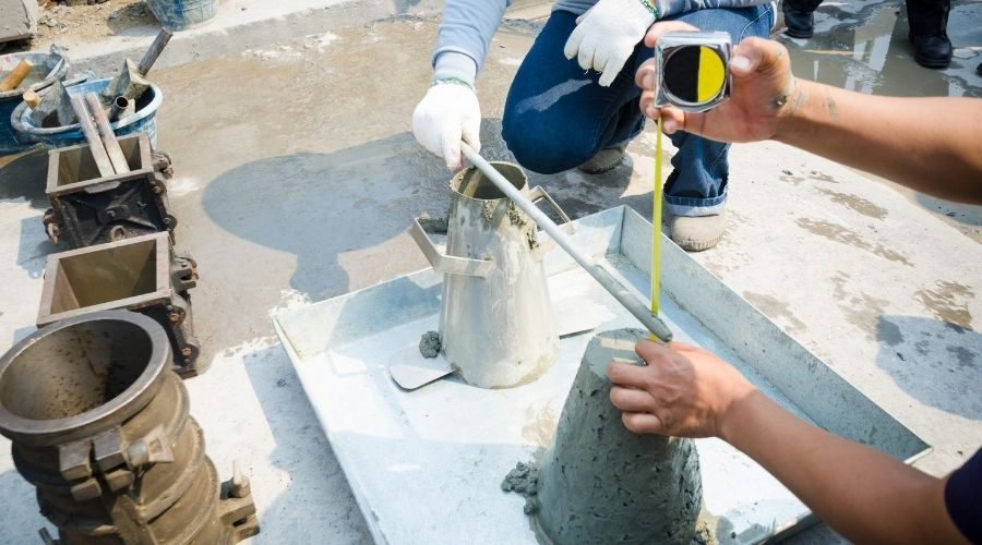A person filling a slump cone with freshly mixed concrete and tamping it with a steel rod