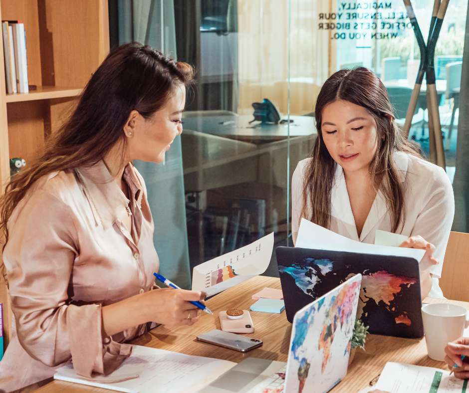 two women examine papers and laptop screens