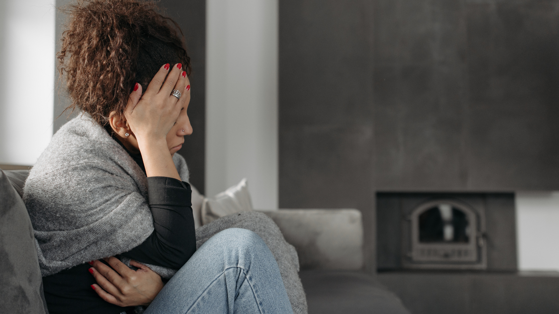 woman sitting on a sofa wrapped in a blanket with her head in her hand