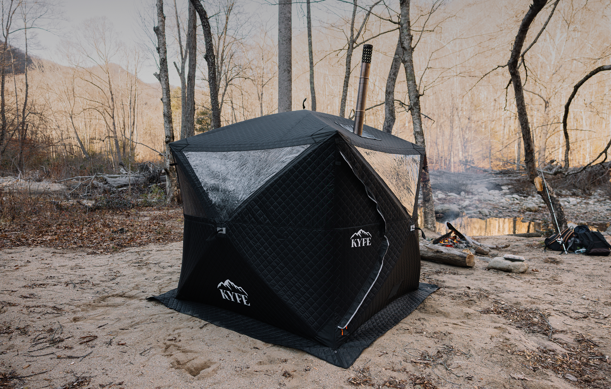 A portable wood-fired sauna tent is set up in a sand clearing, indicating the high temperature inside. This traditional sauna offers a satisfying sauna experience, utilizing a wood-burning stove to create hot air and promote relaxation in the fresh air.