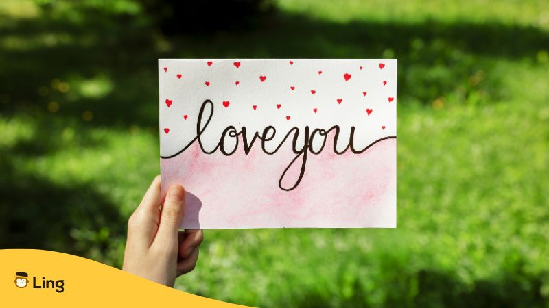 Woman Holding Card with Phrase Love You Outdoors, Closeup