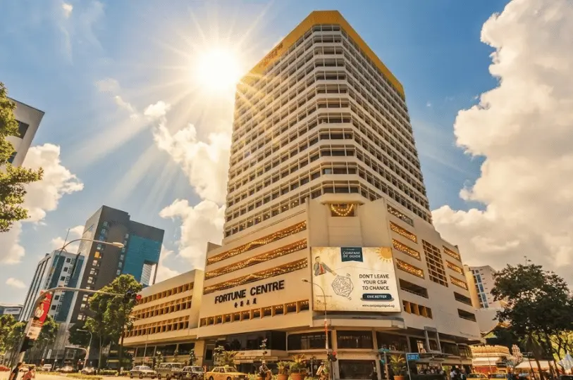 The exterior of the towering Fortune Centre building on a bright, sunny day, with sun rays peeking brilliantly over the top corner of its facade against a blue sky with fluffy clouds.