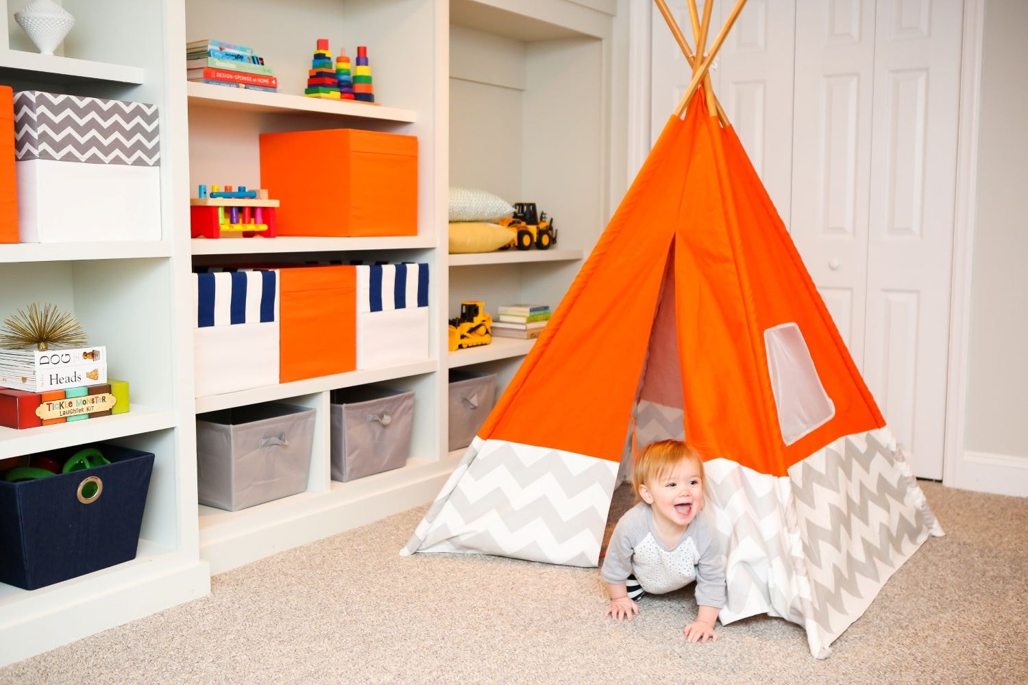 A cosy play area designed for toddlers features child-sized furniture, including a small tent , along with accessible storage bins filled with colourful children's toys and books, creating an inviting space for imagination and fun in a toddler boy's room.