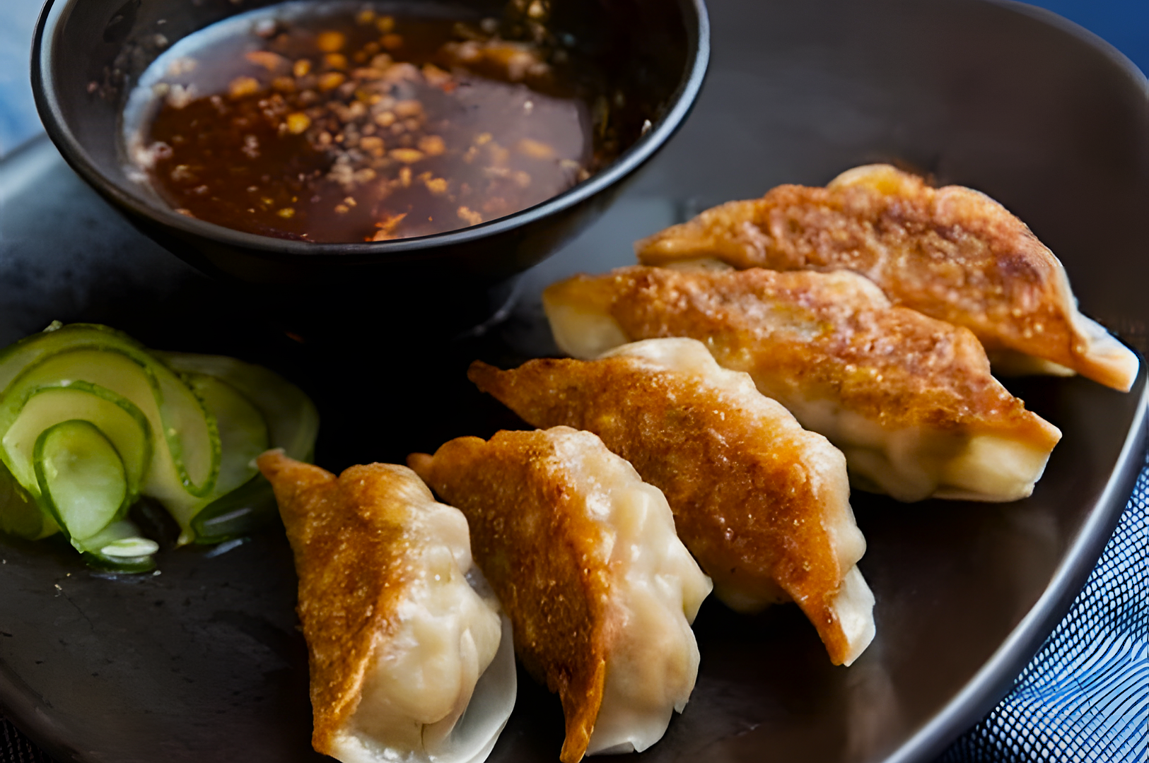 A plate of golden-brown fried dumplings served with a bowl of soy-based dipping sauce and sliced cucumber garnish, exuding a warm, appetizing vibe.