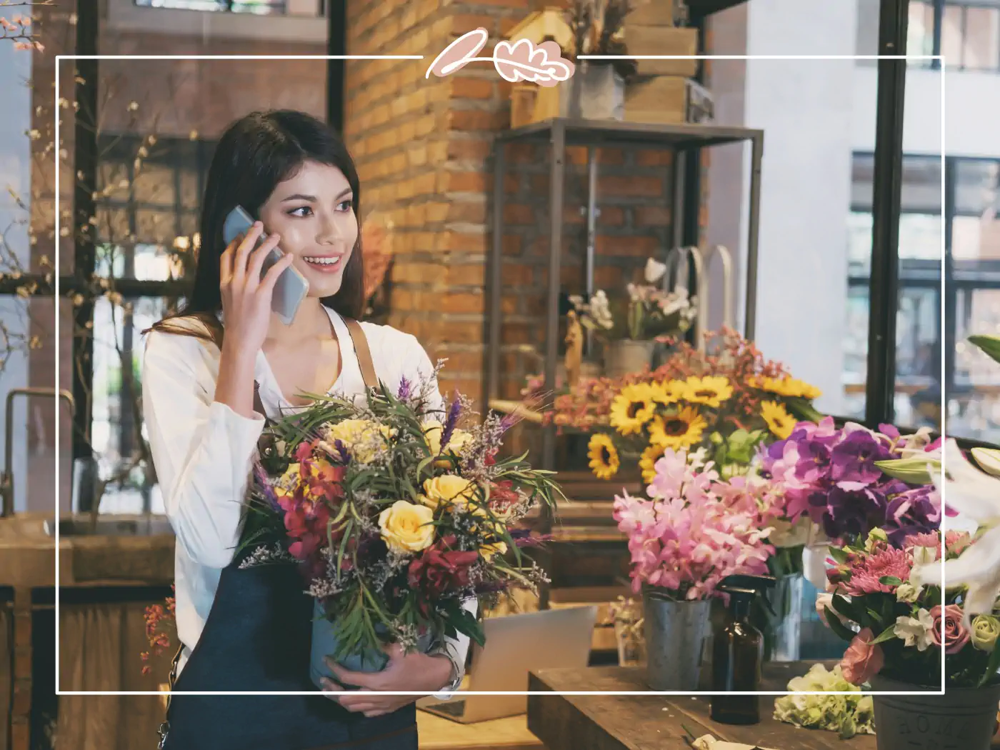 Smiling female florist on the phone holding a bouquet of colorful flowers in a flower shop, Fabulous Flowers and Gifts