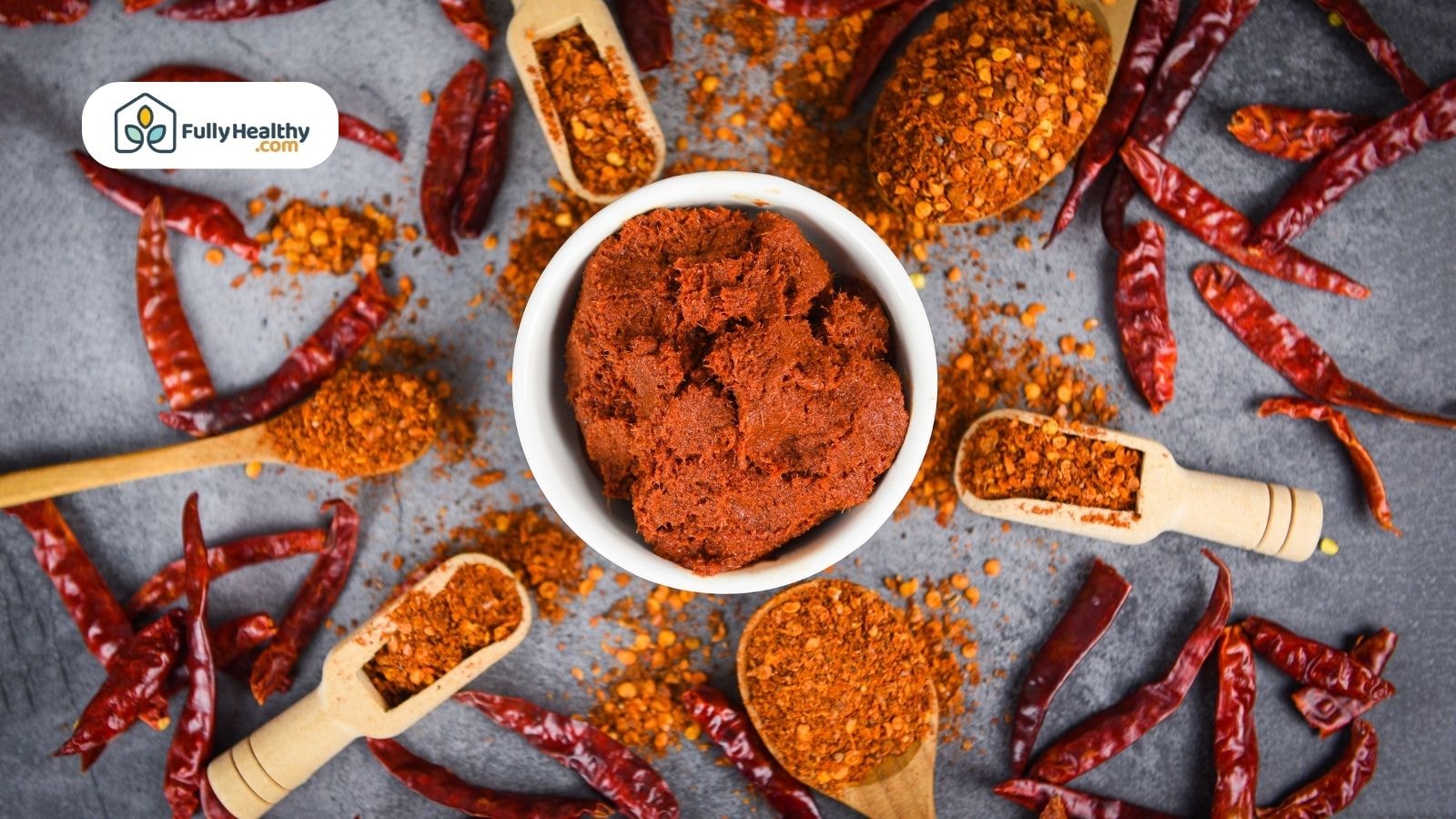 Red dried chili peppers and chili powder scattered around a bowl of chili paste