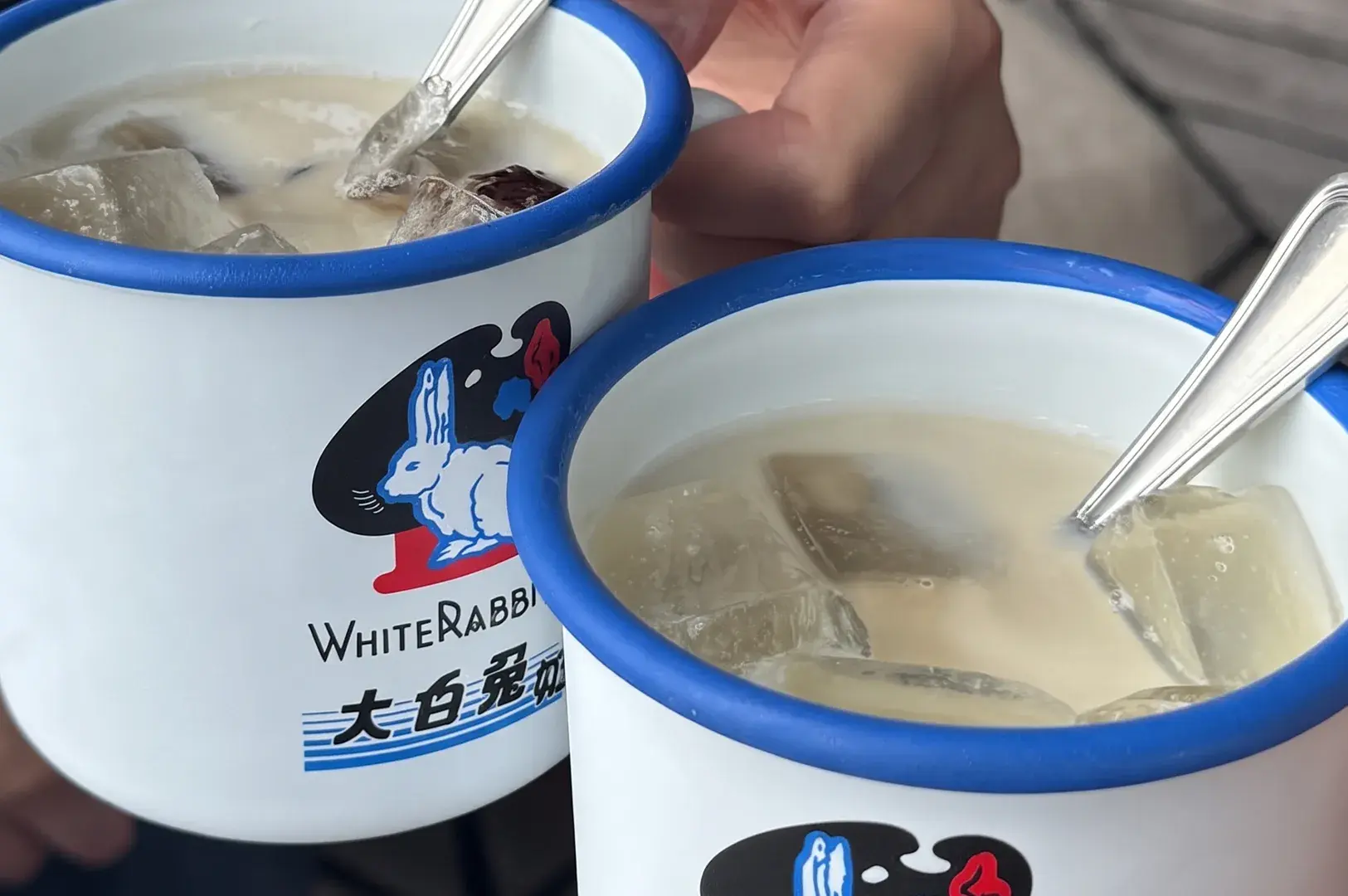 Two White Rabbit logo enamel mugs filled with iced milky drinks and spoons.