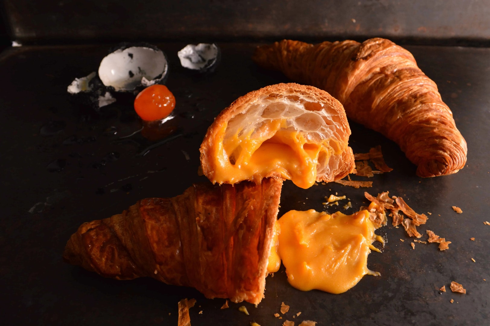 A croissant filled with cheese and eggs, presented on a black surface, showcasing a viral Singapore fusion food trend.