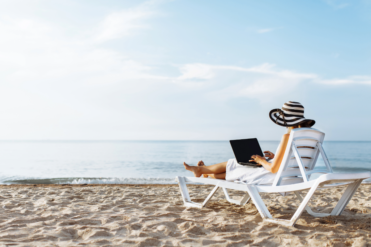 Woman in a sun hat sitting on a lounge chair with a laptop on a quiet Jersey Shore beach, enjoying remote work during a winter monthly rental stay.