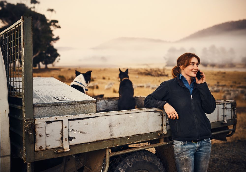 Young woman with dark hair leaning against a farm truck talking on a cell phone.   