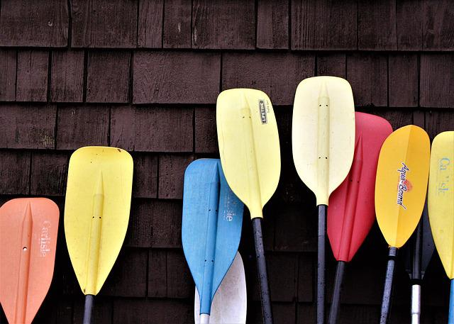 Paddles and oars leaning in front of a shingled wall. 