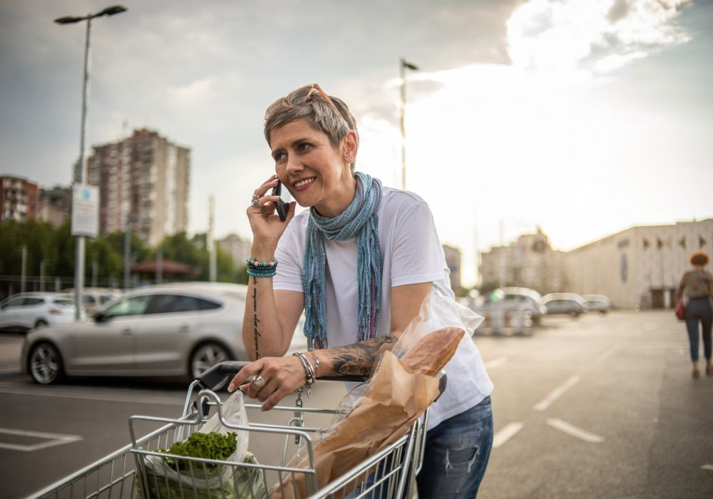 Short haired blonde woman talking on her cell in a supermarket parking lot.