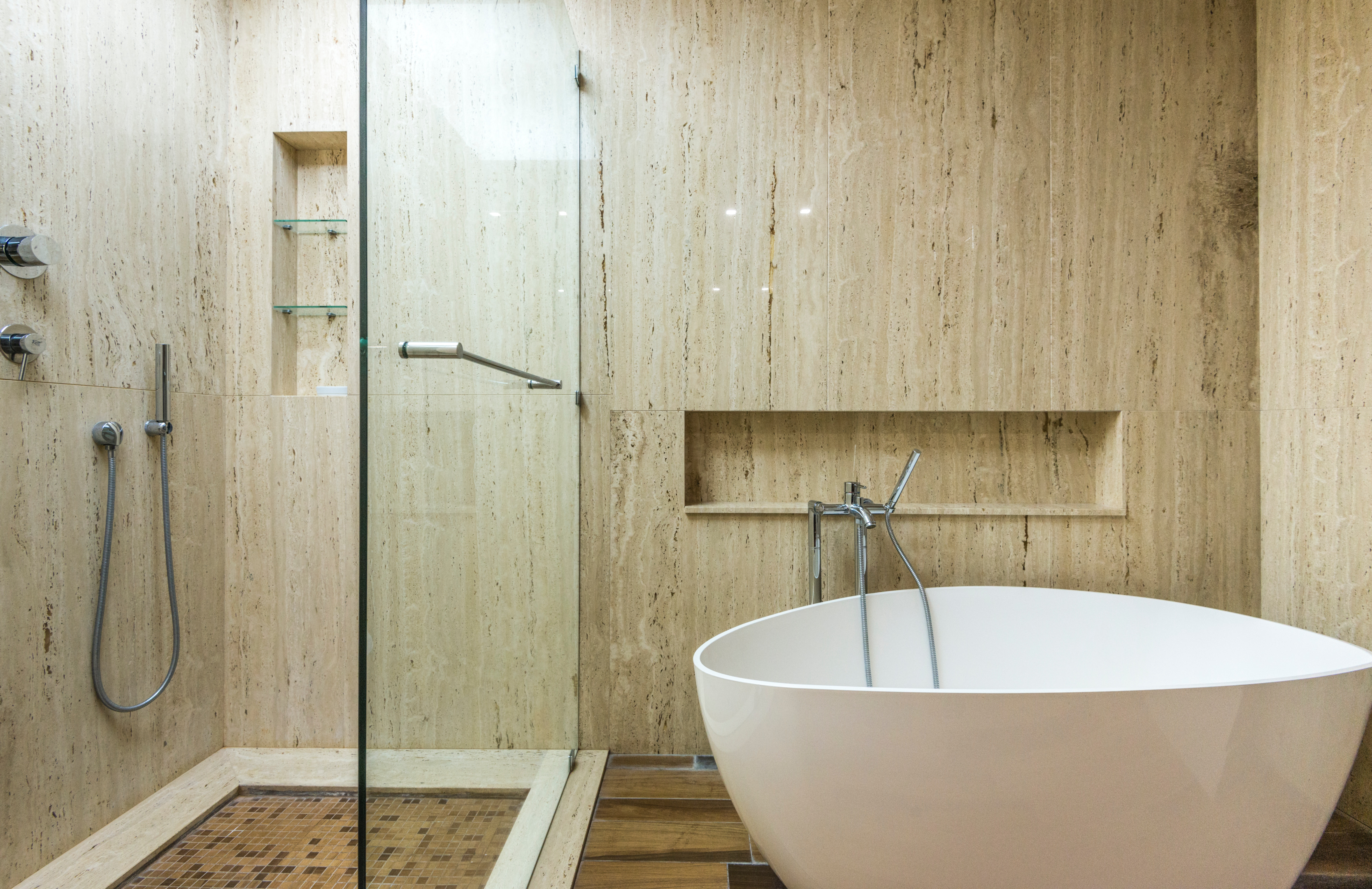 large modern bathtub with shower niche shelf next to walk-in shower with glass shelving niche