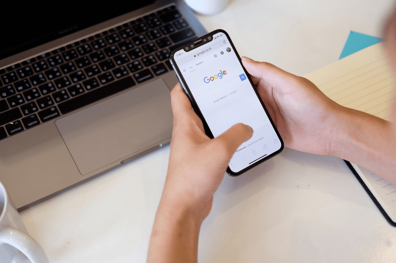 A person holding a smartphone showing the Google search homepage next to a laptop, highlighting mobile visibility for local dining searches.