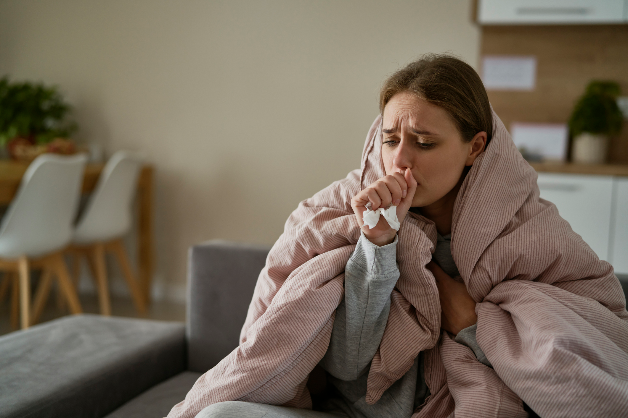 An image of a sick woman with a blanket around her shoulders and a tissue in her hand. 