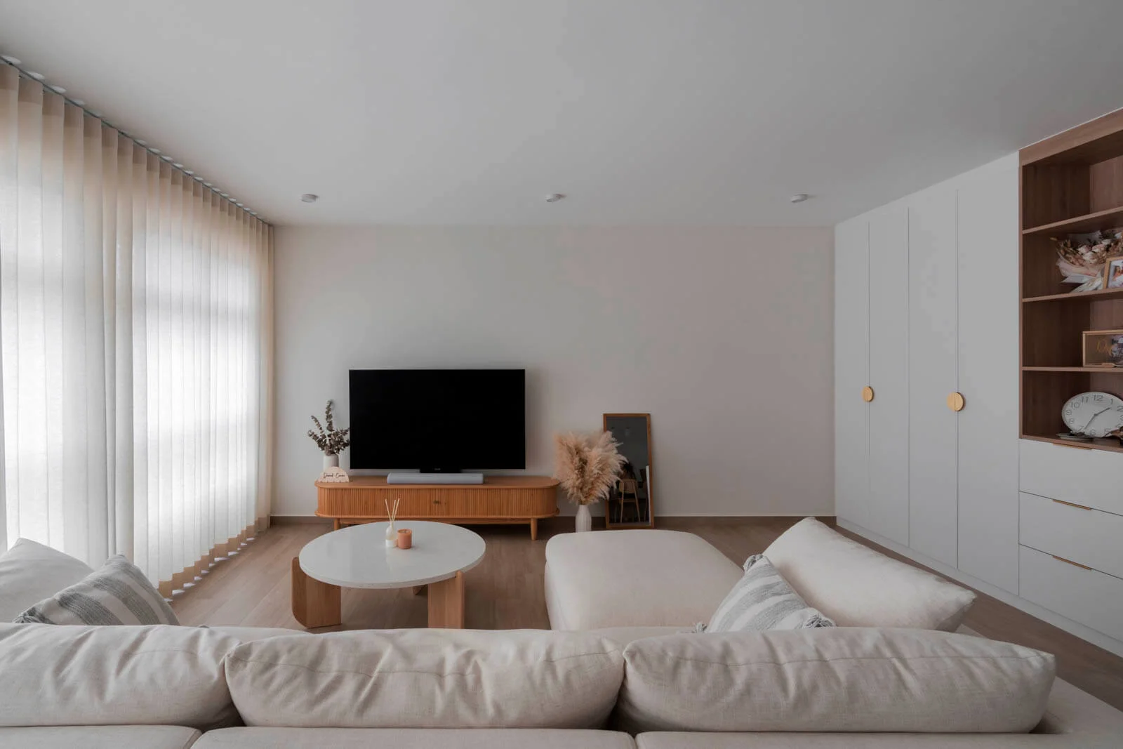 Warm minimalist lounge with wooden TV console, sheer curtains and neutral modular sofa