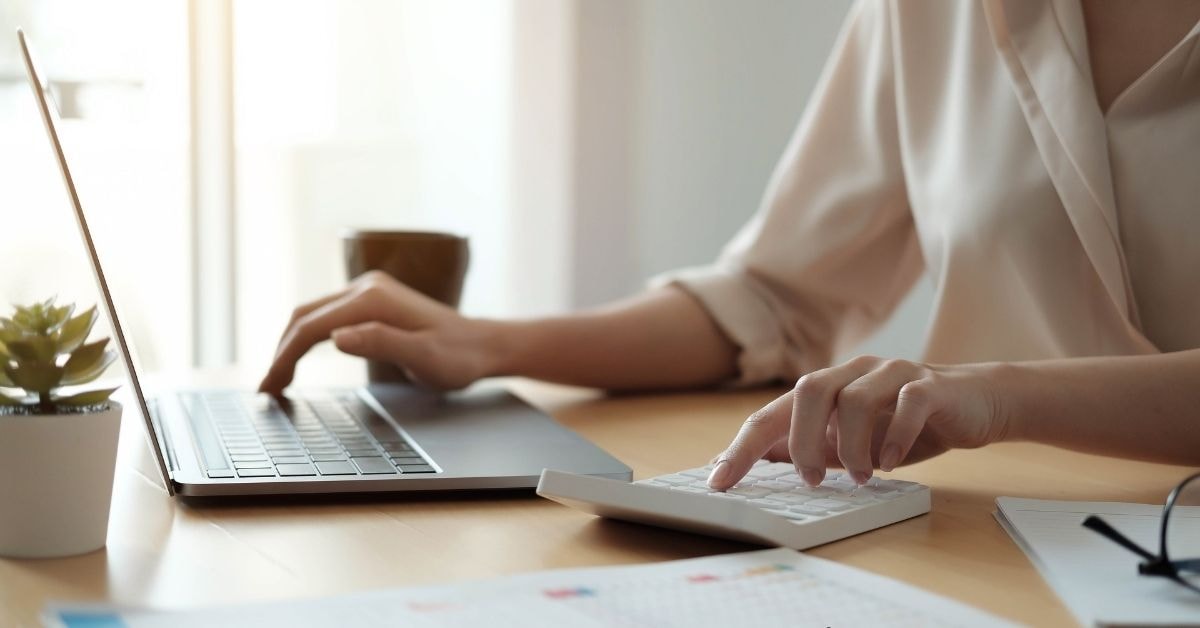 A person using a laptop and calculator to manage expenses, possibly organizing a detailed payment report.