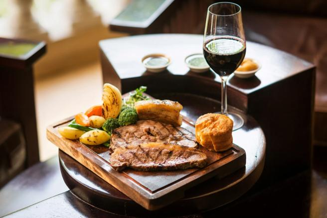 Photograph of a traditional British roast served on a wooden platter with a glass of red wine