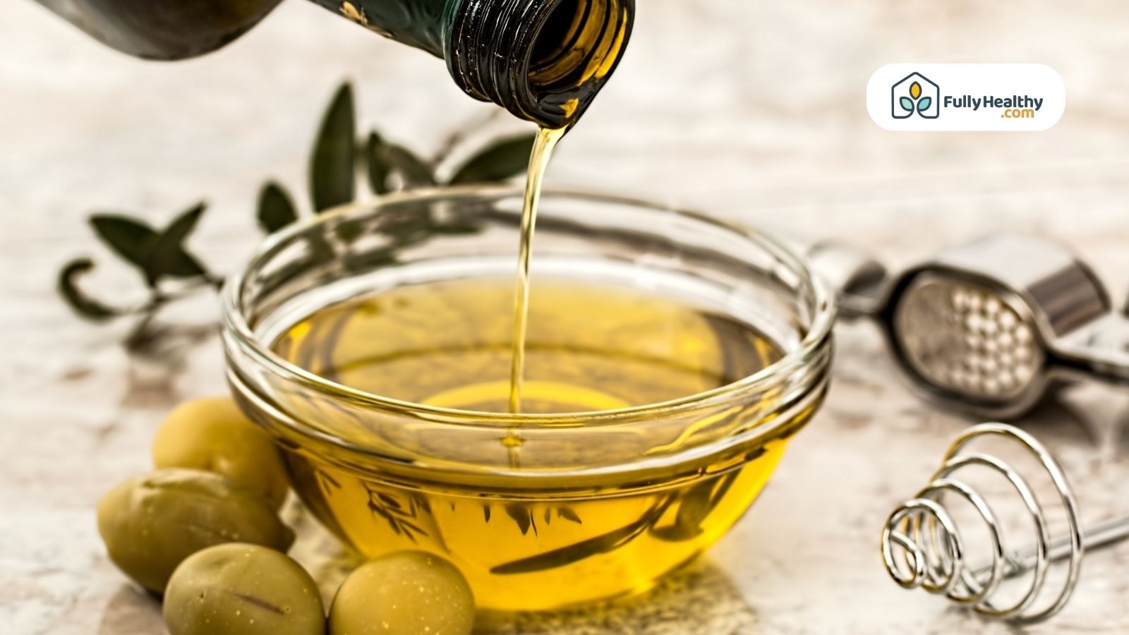 Olive oil being poured into a glass bowl with fresh olives