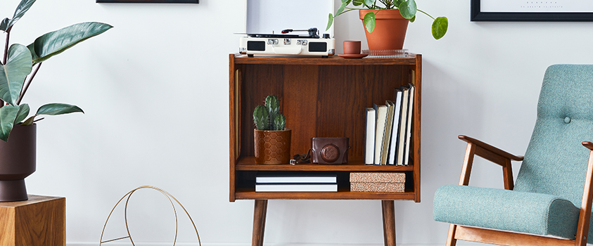 A side table holding a few books, a vintage camera, two plants and a record player. To the right is a grey/green armchair.