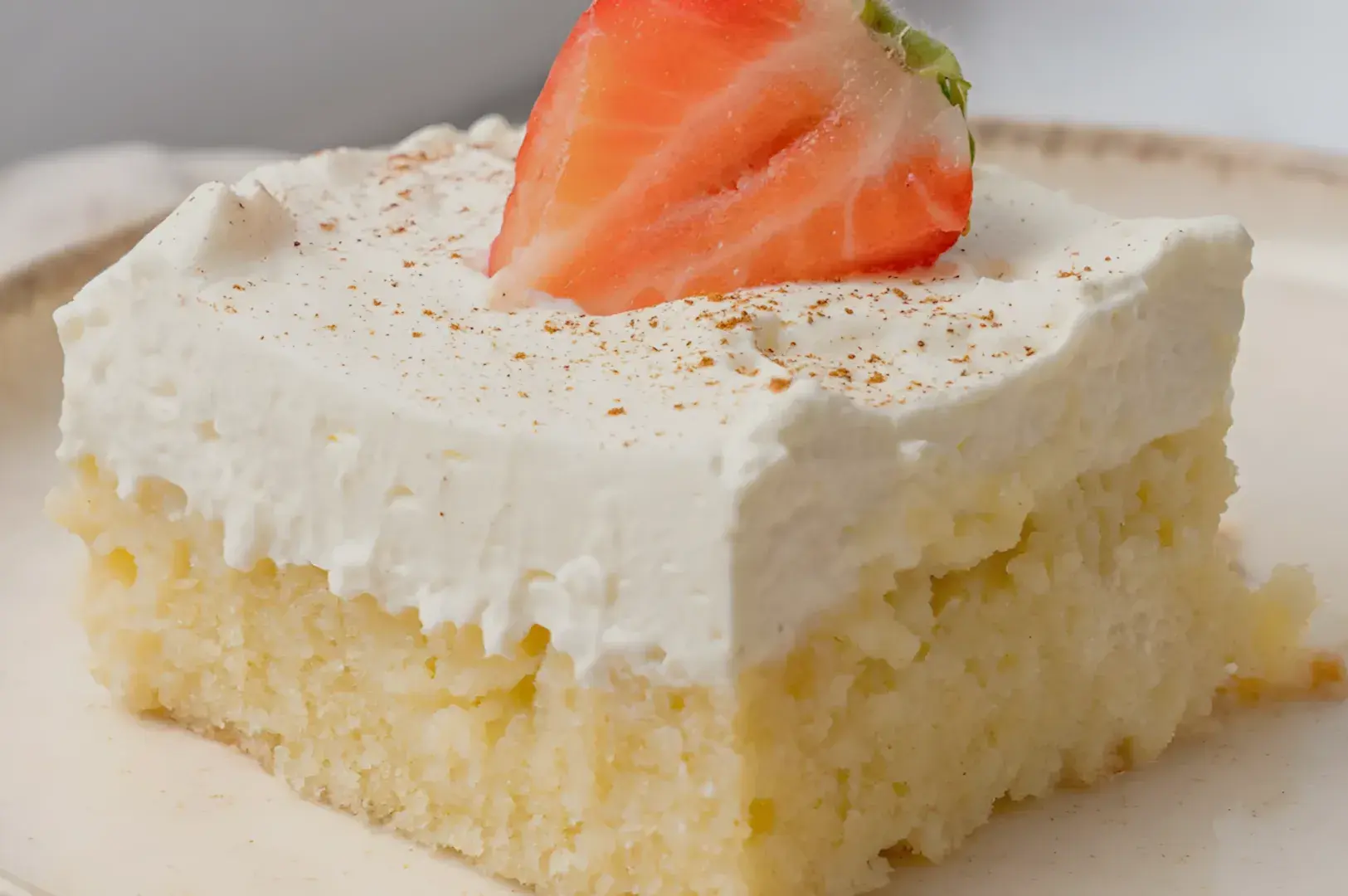 A piece of cake topped with whipped cream and a slice of strawberry.