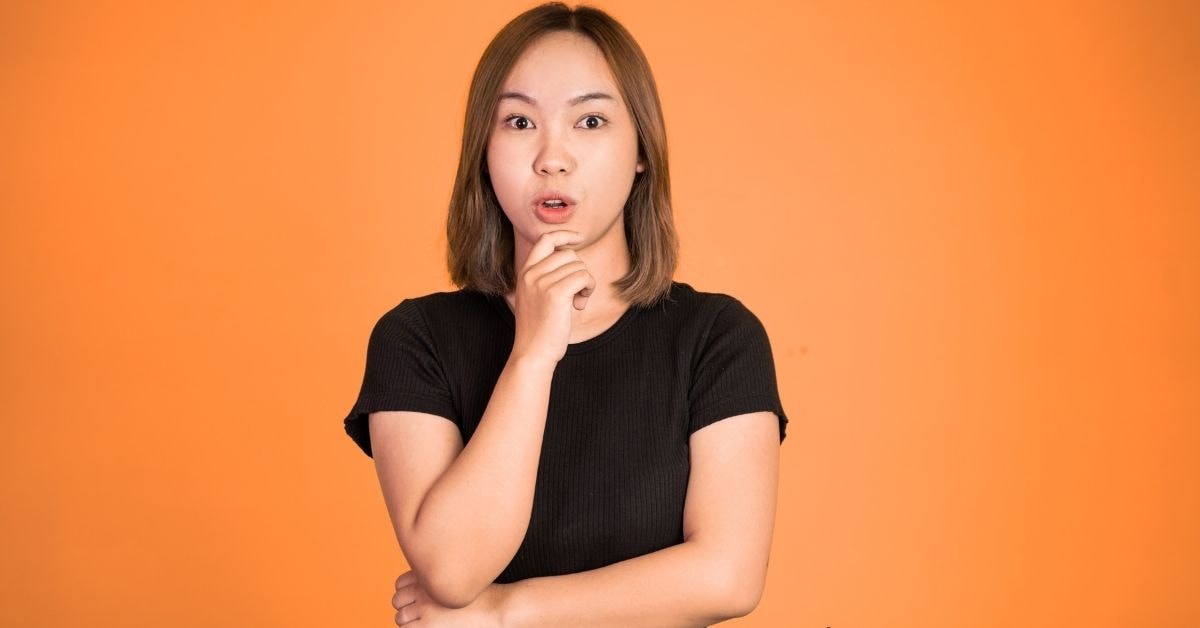 Surprised creator in black shirt, contemplating her tax plan against an orange background.