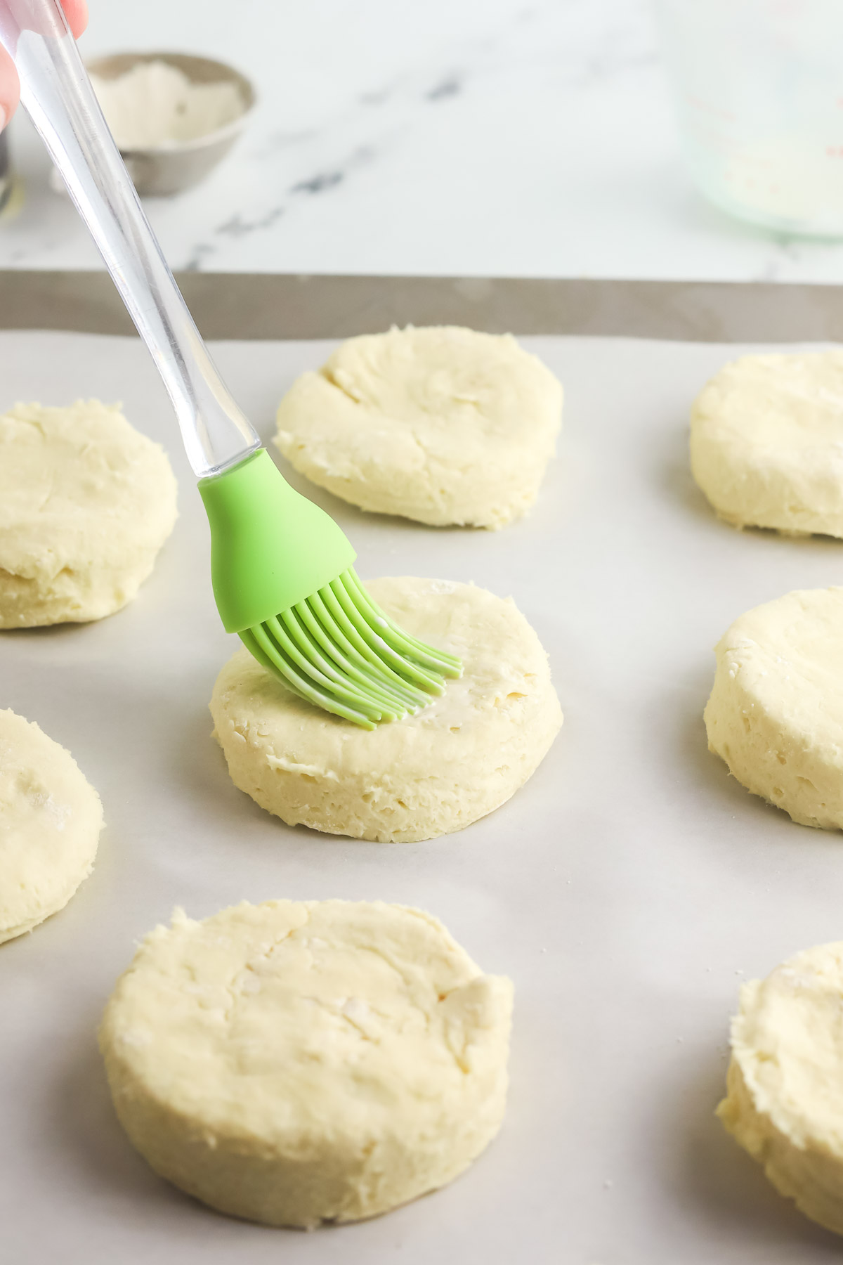 silicone brush brushing on heavy cream on top of cream biscuits before baking