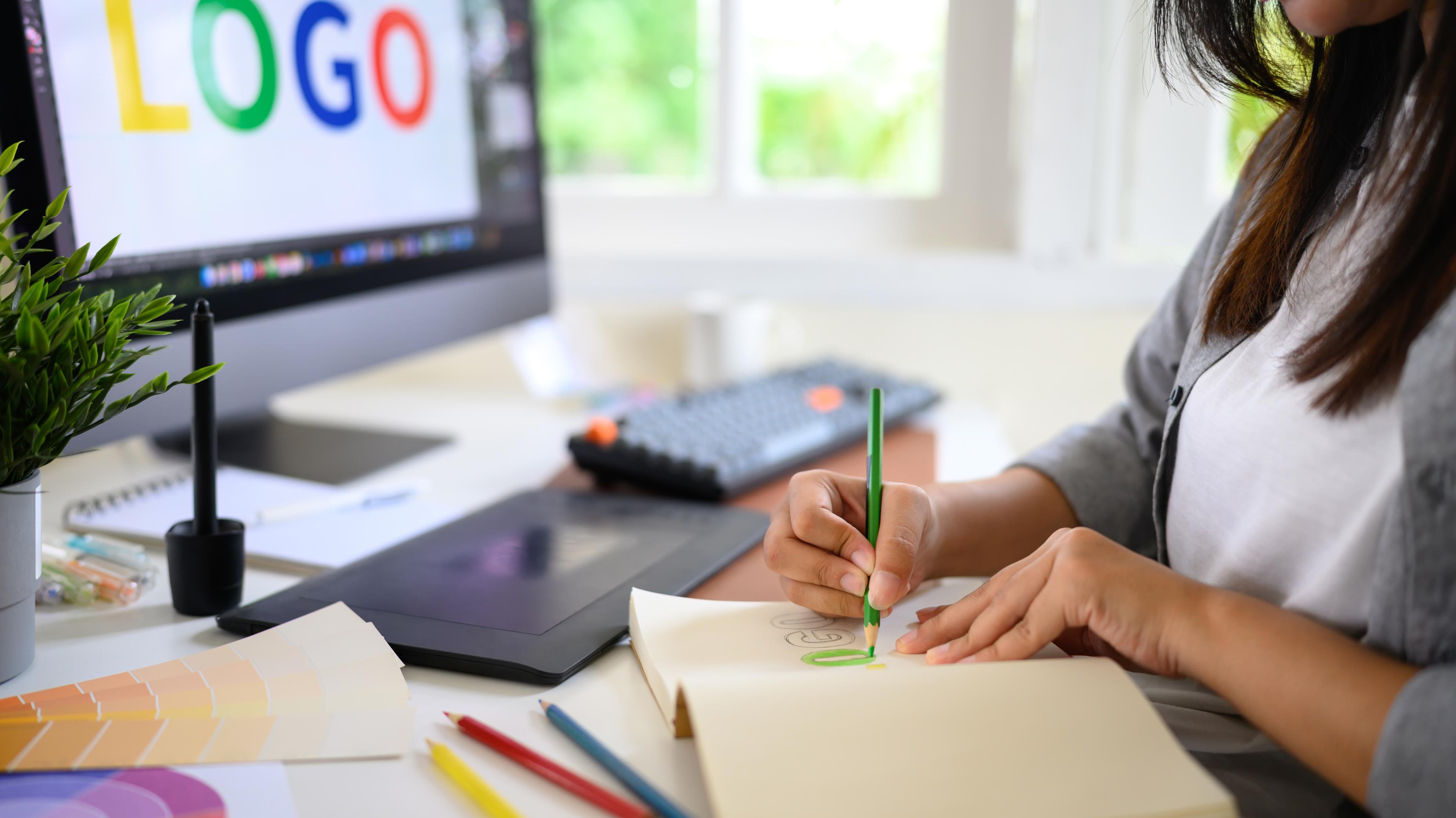 Gros plan d'une femme créative esquissant des idées de logos dans un carnet avec des échantillons de couleur et des crayons