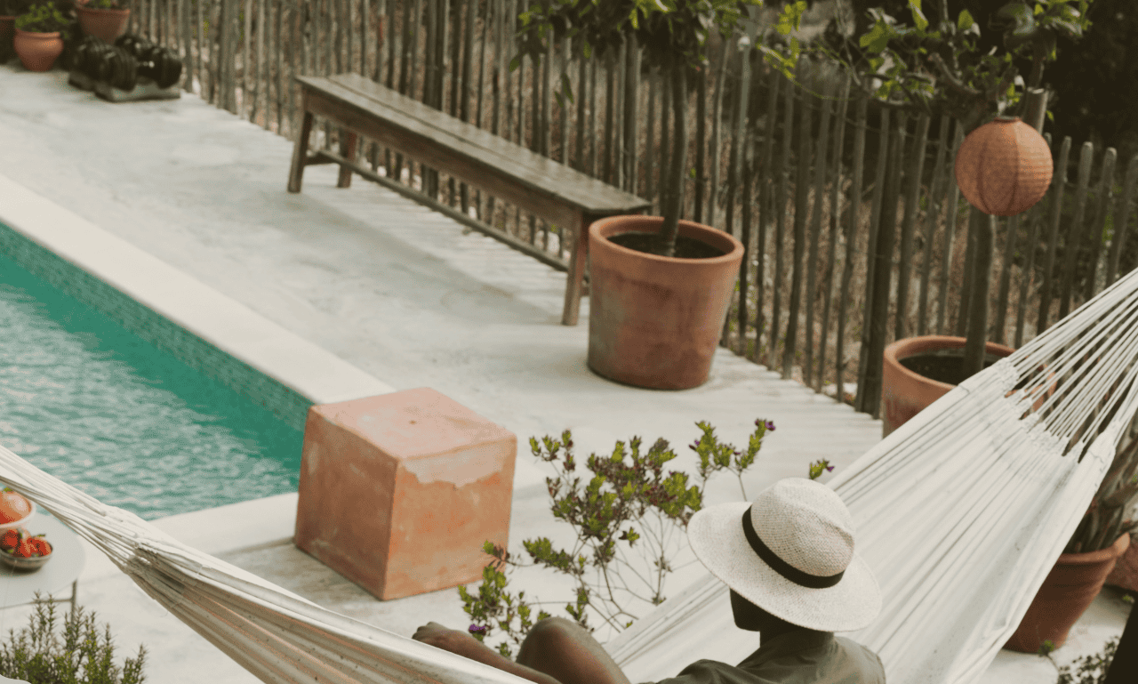 A man sitting by the pool in a hammock.