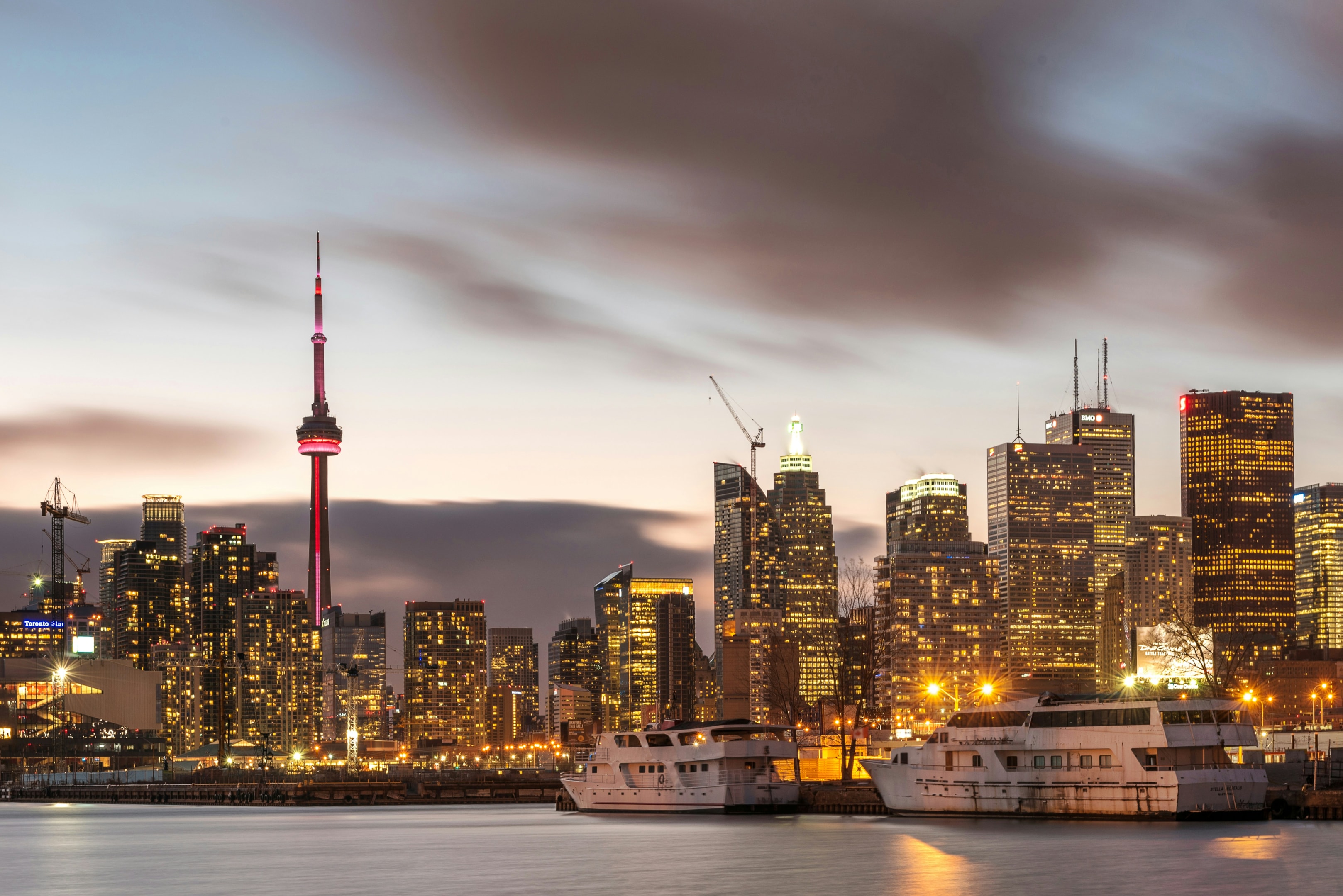 Image: An image of the Toronto, Ontario skyline at dusk featuring the waterfront and CN Tower.